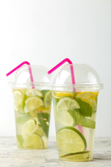 Mojito cocktail in a plastic glass with lime, mint and lemon on a light concrete table. make a mojito.