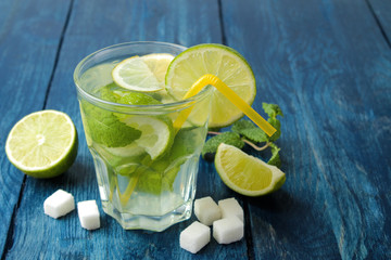 Mojito cocktail in a glass glass with lime, mint and lemon on a blue wooden table. make a mojito.