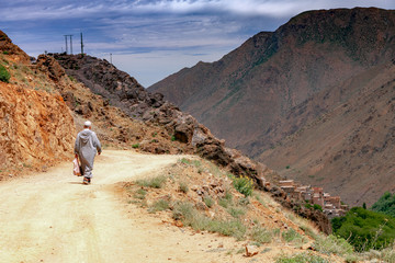 Marokański góral idzie po piaszczystej drodze między górskimi miejscowościami 