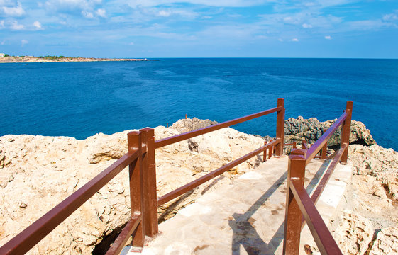 A stone path with brown railings leading to deep blue azure water