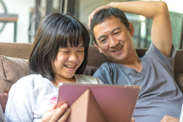 Father and daughter concept. Daddy working on computer notebook hand typing on keyboard while Asia kid girl using tablet hand touching on touchscreen playing game.