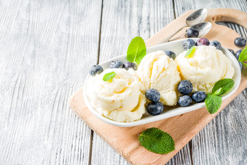 White vanilla ice cream balls with ice cream cones, spoon, fresh blueberry berries and mint leaves, rustic wooden background copy space