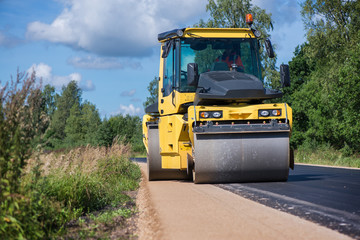 Yellow heavy vibration roller at asphalt pavement works. Road repairing in city. Road construction workers repairing highway road on sunny summer day. Heavy machinery, loaders and trucks. 