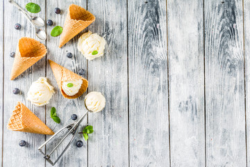 White vanilla ice cream balls with ice cream cones, spoon, fresh blueberry berries and mint leaves, rustic wooden background copy space