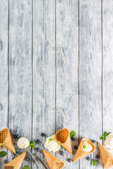 White vanilla ice cream balls with ice cream cones, spoon, fresh blueberry berries and mint leaves, rustic wooden background copy space