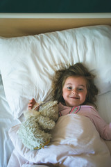 Little girl lying in a bed with teddy bear at the morning