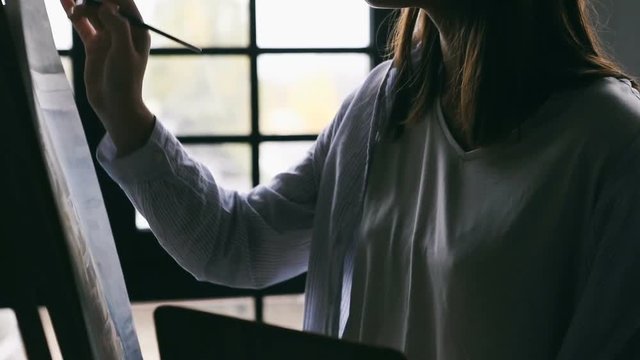 Artist young woman is painting. Backlight close up. Relaxed creative atmosphere. Video footage.