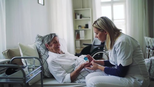A health visitor giving pills to a sick senior woman lying in bed at home.