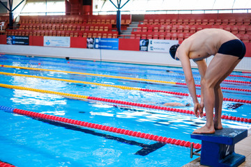 Muscular swimmer preparing to jump from starting block in a swimming pool