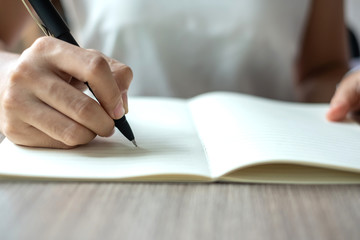 Businesswoman writing on notebook in office, hand of woman holding pen with signature on paper report. business concepts