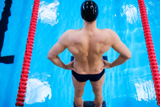 Muscular swimmer preparing to jump from starting block in a swimming pool