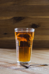glass of herbal tea on wooden table with sugar sprinkled next to it