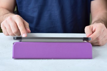 White man‘s hands holding a new tablet and put on a purple leather case with selective focus. Man using a tablet. Putting on a violet protection cases for personal tablet. Tablet accessories 