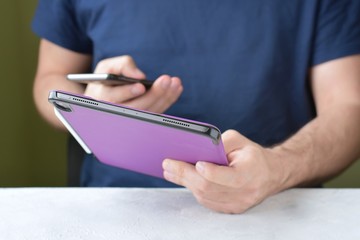 White man‘s hands holding a new tablet and put on a purple leather case with selective focus. Man...