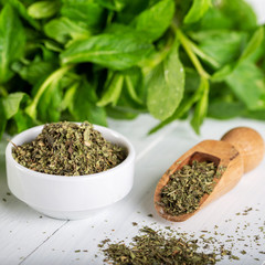 Dried peppermint in a white bowl and a bunch of fresh mint, on wooden background. Food background.