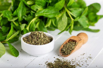 Dried peppermint in a white bowl and a bunch of fresh mint, on wooden background. Food background.