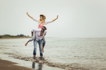 Happy couple in love on beach summer vacations. Joyful girl piggybacking on young boyfriend having fun.