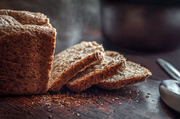 Closeup of fresh homemade organic whole grain bread with crispy crust and warm steam cut into slices on a rustic kitchen table with crumbs in the countryside