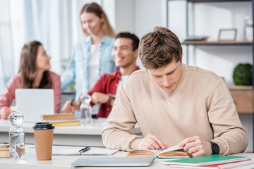 Fototapeta premium Concentrated student sitting at desk and reading book in classroom