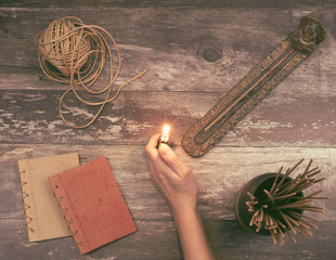 Woman hand lights a incense stick from a Buddha holder on a vintage natural wooden surface with books, hemp twine and many aromatic smelling incense sticks - Concept of spiritual ritual, creativity