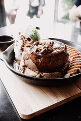 Delicious pancake with banana chocolate and vanilla ice cream on black iron pan over cock coaster.