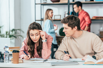 Two students talking and writing in notebooks at table