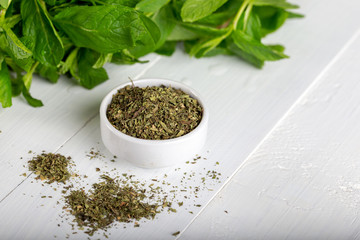 Dried peppermint in a white bowl and a bunch of fresh mint, on wooden background. Food background.