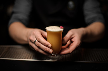 Professional bartender serving a cocktail in the glass with foam decorated with a one red rose bud