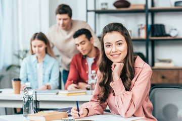 Pretty student writing in notebook and looking at camera