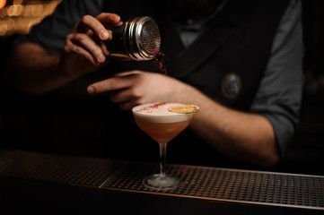 Professional bartender holding a spice shaker adding to a delicious cocktail red flavours