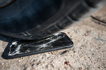 Broken and damaged smartphone with cracks on glass screen laying on ground. Accident. Cell phone under car wheel. Concept of warranty and lost smartphone 