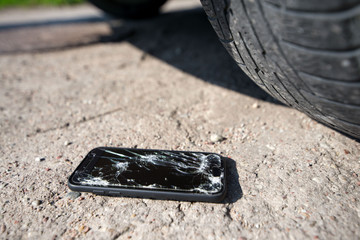 Broken and damaged smartphone with cracks on glass screen laying on ground. Accident. Cell phone under car wheel. Concept of warranty and lost smartphone 