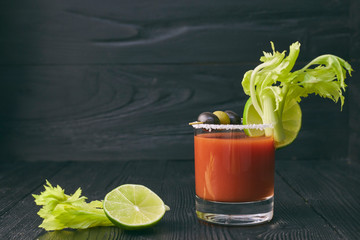 Bloody mary cockCocktail Bloody Mary with lime and celery, salt and snacks in a glass on a black wooden table. horizontal view of a cocktail.tail