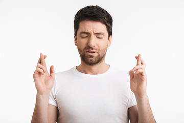 Image of upset man 30s with bristle in casual t-shirt keeping fingers crossed and making a wish