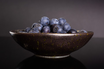 Lot of whole fresh sweet purple blueberry american in a grey ceramic bowl isolated on black glass