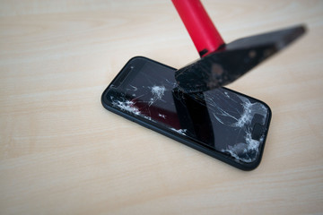 Hammer cracking on smartphone. Screen and display is destroyed, damaged and cracked. Concept of anger, rage and repairing electronic devices. Valid warranty