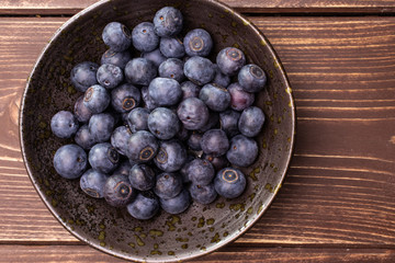 Lot of whole fresh sweet purple blueberry american in a grey ceramic bowl flatlay on brown wood