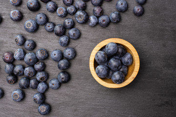 Lot of whole fresh sweet purple blueberry american with wooden bowl flatlay on grey stone