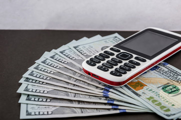 push-button mobile phone on a gray background and hundred dollar bills