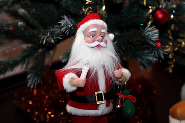 Santa Claus. A doll of New Year's Santa Claus with a candle in his left hand and a red cap stands against the backdrop of a Christmas tree.