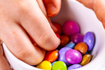Child eating chocolate lentels from white bowl