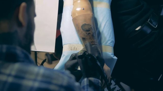 Tattoo master creating a tattoo on a hand prosthesis, artificial arm.