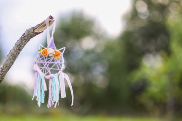 Colorful dreamcatcher outdoors on summer nature background. Handmade decor made of feathers, ribbons, threads and beads