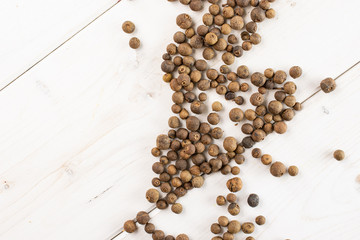 Lot of whole dry brown allspice berries flatlay on white wood