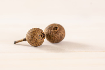 Group of two whole dry brown allspice berries on white wood