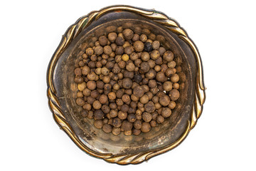 Lot of whole dry brown allspice berries in a brown iron pan flatlay isolated on white background