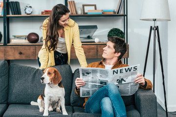 Man with dog reading newspaper on sofa and looking at girl