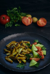 Freshly cooked fried potatoes with onions and mushrooms close-up on a plate. ebony table. vertical view of the dish.