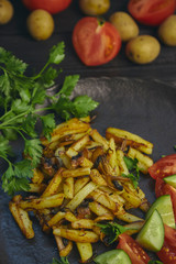 Freshly cooked fried potatoes with onions and mushrooms close-up on a plate. ebony table. vertical view of the dish.