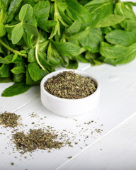 Dried peppermint in a white bowl and a bunch of fresh mint, on wooden background. Food background.